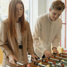 Two young adults enjoying a game of table football in a bright indoor setting.